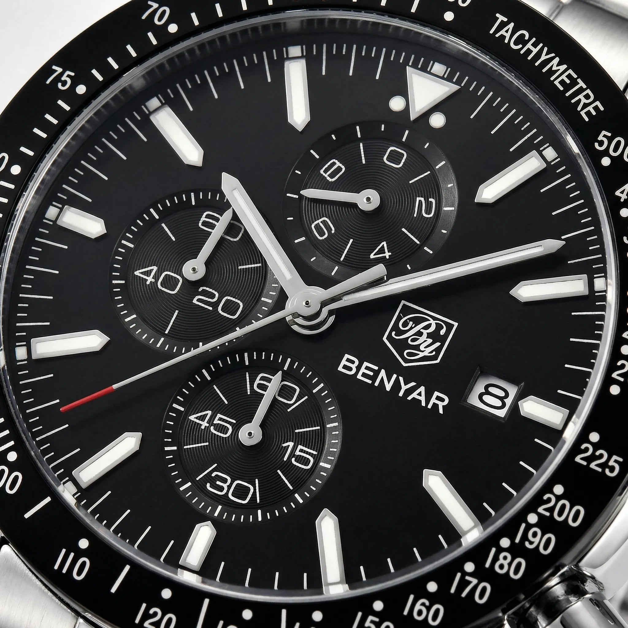 Close-up of the luminous hands and markers on a black dial racing chronograph watch.